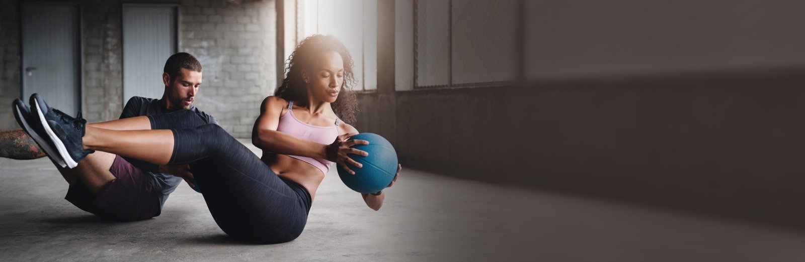 Hombre y mujer haciendo abdominales en pareja con un balón medicinal durante una sesión de entrenamiento funcional